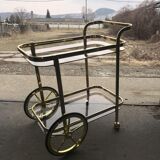 Two-tier bar cart in gold-plated brass with transparent glass shelves, yellow finish.