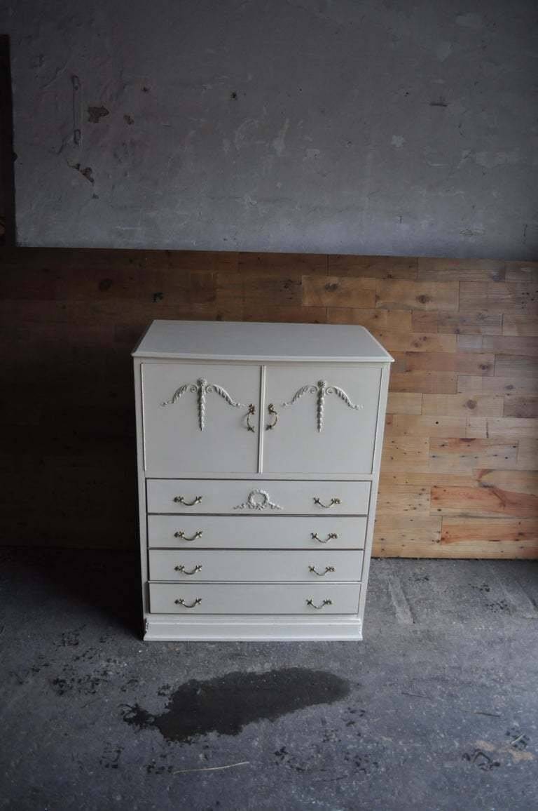 Mid-century wooden dresser painted in cream white, with 2 doors and 4 drawers, brass fittings.