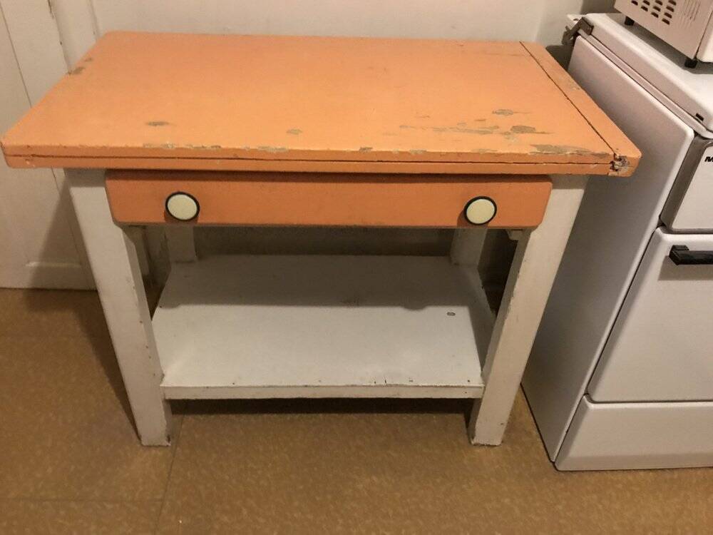 Vintage wooden kitchen table in orange and white with a drawer and low shelf.