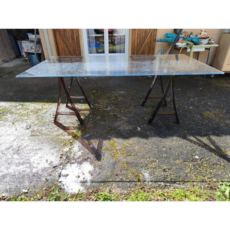 Vintage table with a glass top and smoked plastic trestle legs.