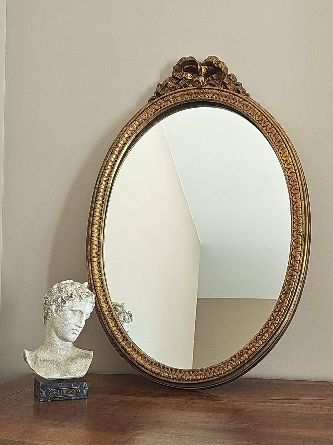 Vintage oval mirror with a carved wooden frame in gold, decorated with a bow.