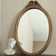 Vintage oval mirror with a carved wooden frame in gold, decorated with a bow.