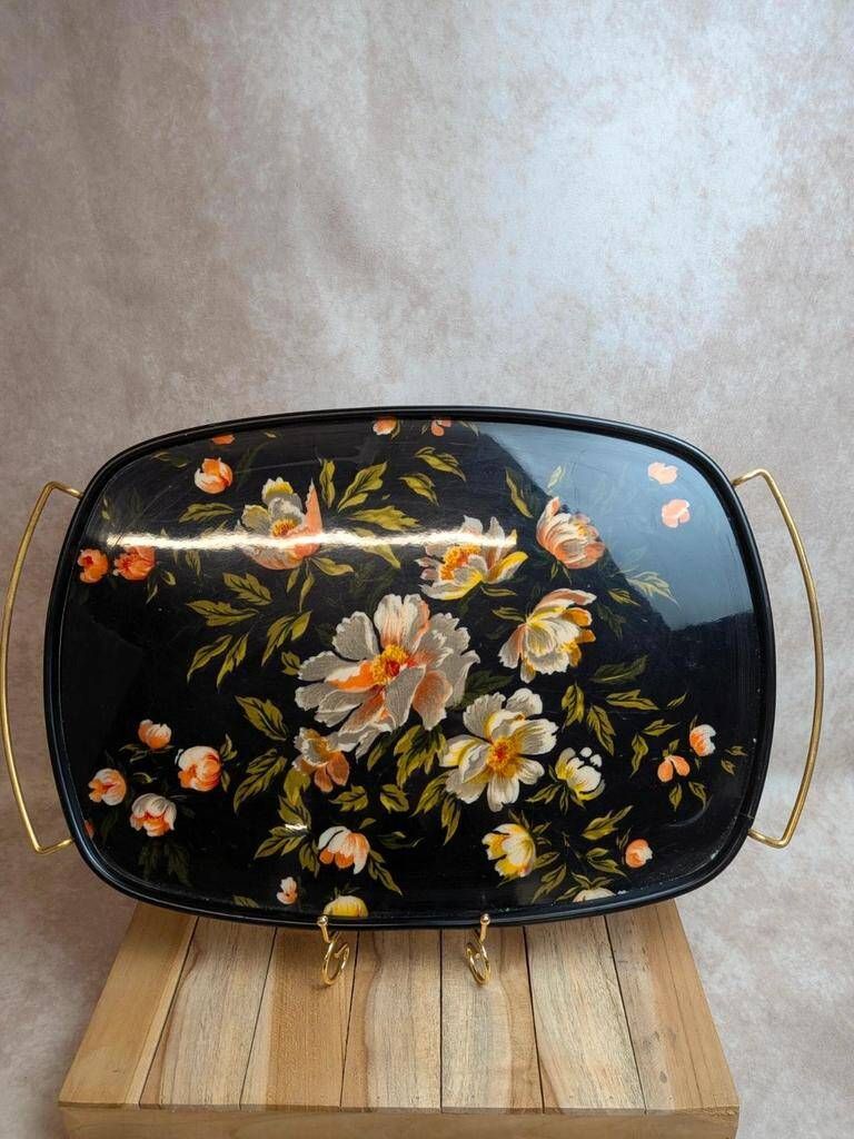 Large vintage 1960s platter with floral decoration on a black background and golden handles.