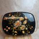 Large vintage 1960s platter with floral decoration on a black background and golden handles.