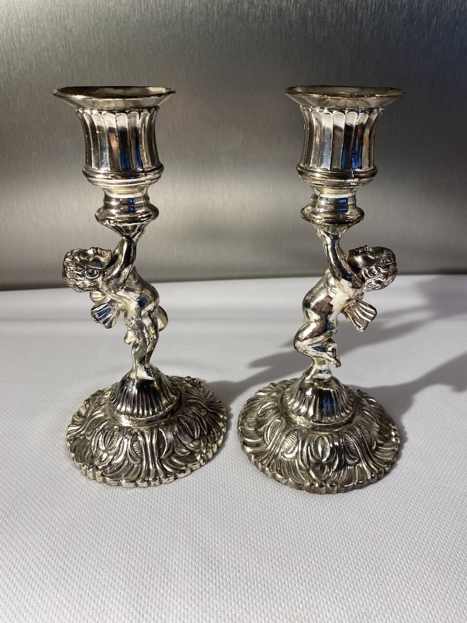 Two silver-plated metal candlesticks decorated with cherubs, 20th century