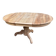 Round extendable dining table stripped in solid raw walnut with a central leg.