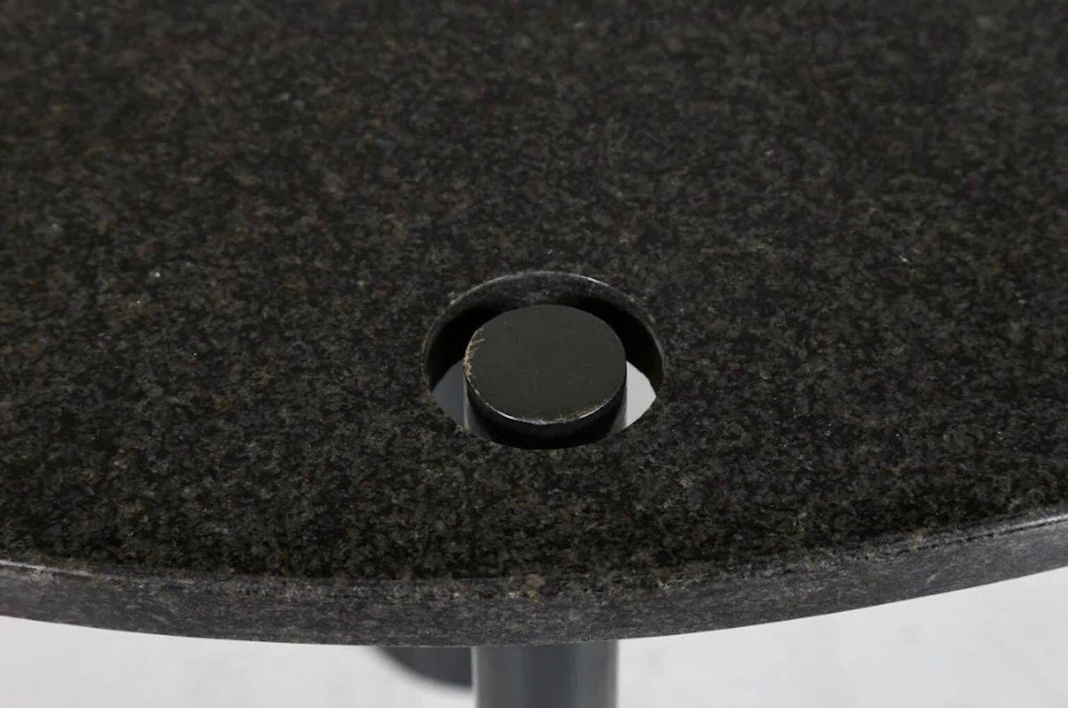 Round dining table in black lacquered metal with a granite top.