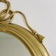 Decorative oval mirror in brass adorned with a large twisted bow.