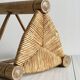Antique tripod stool in light wood with a woven straw seat.