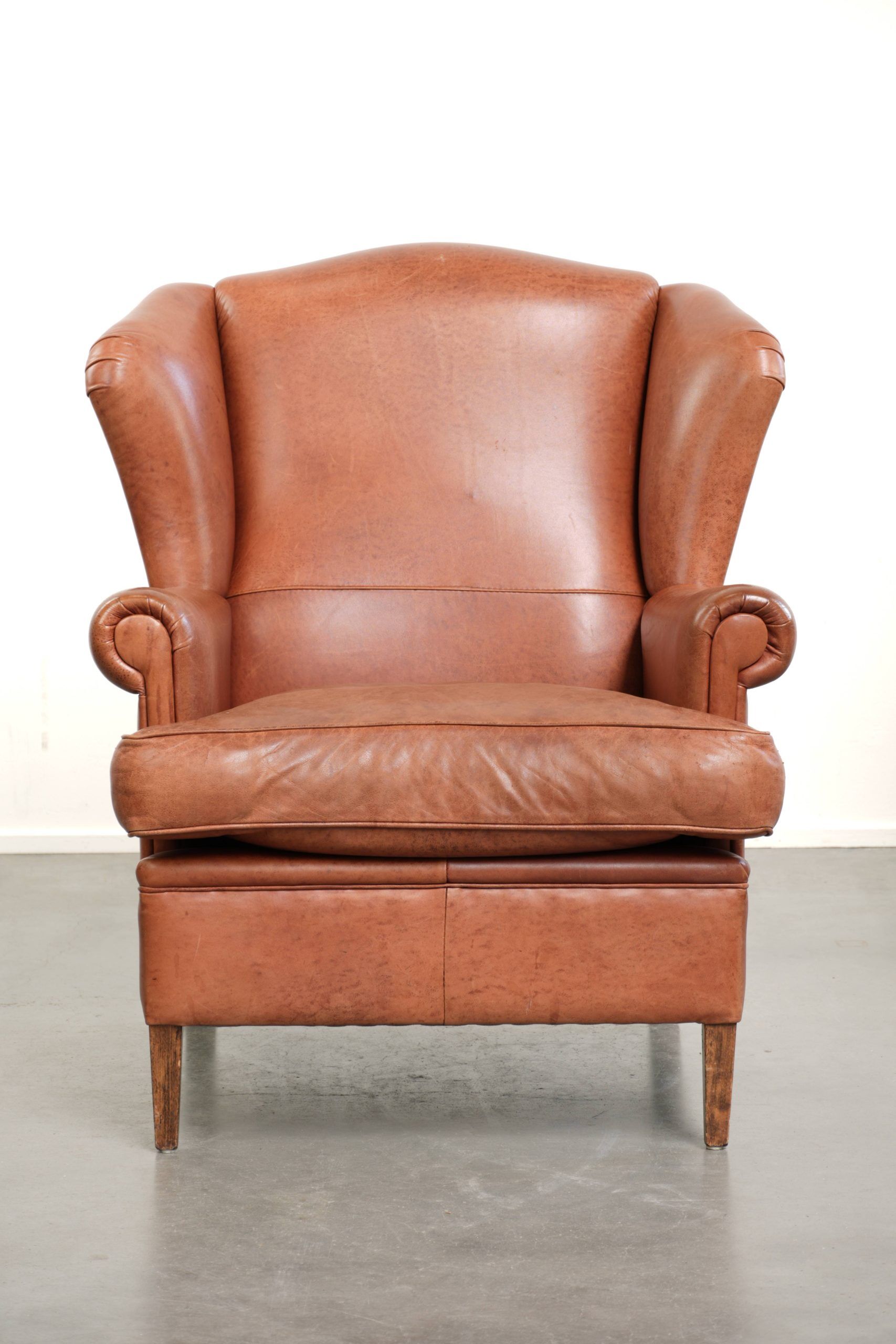 Fauteuil anglais à oreilles de couleur cognac clair en cuir de vache.