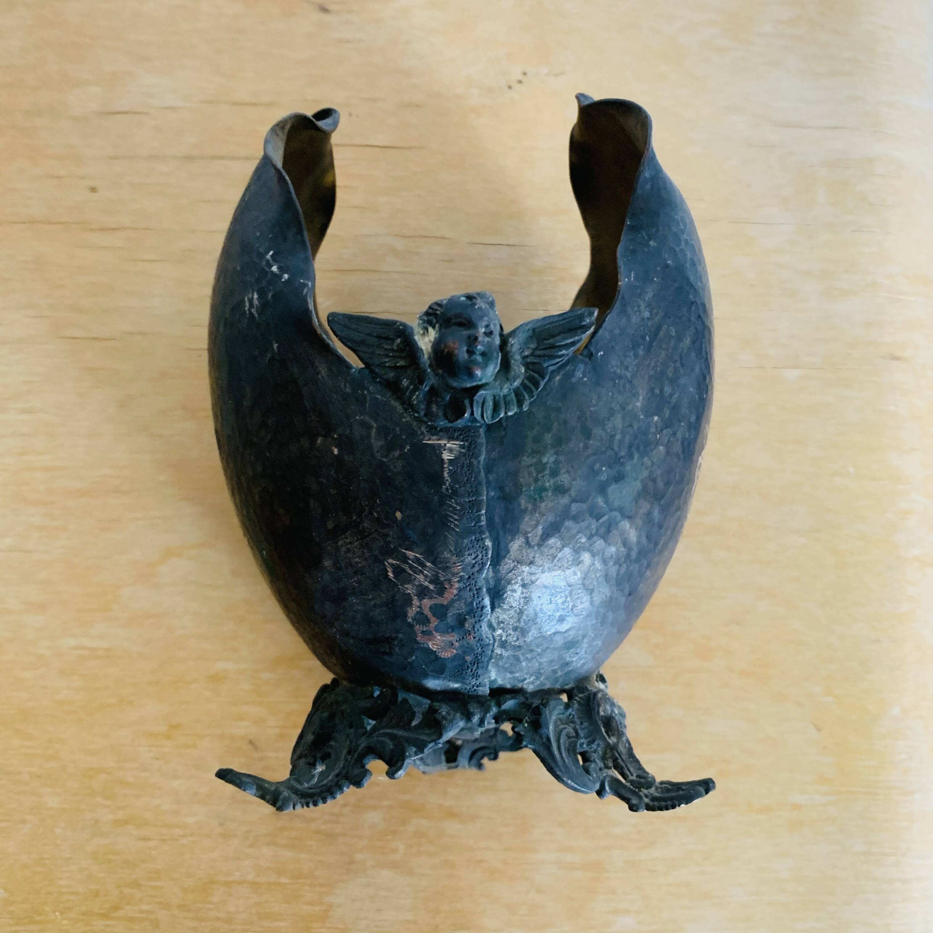 Antique decorative cup in hammered metal with putto design.