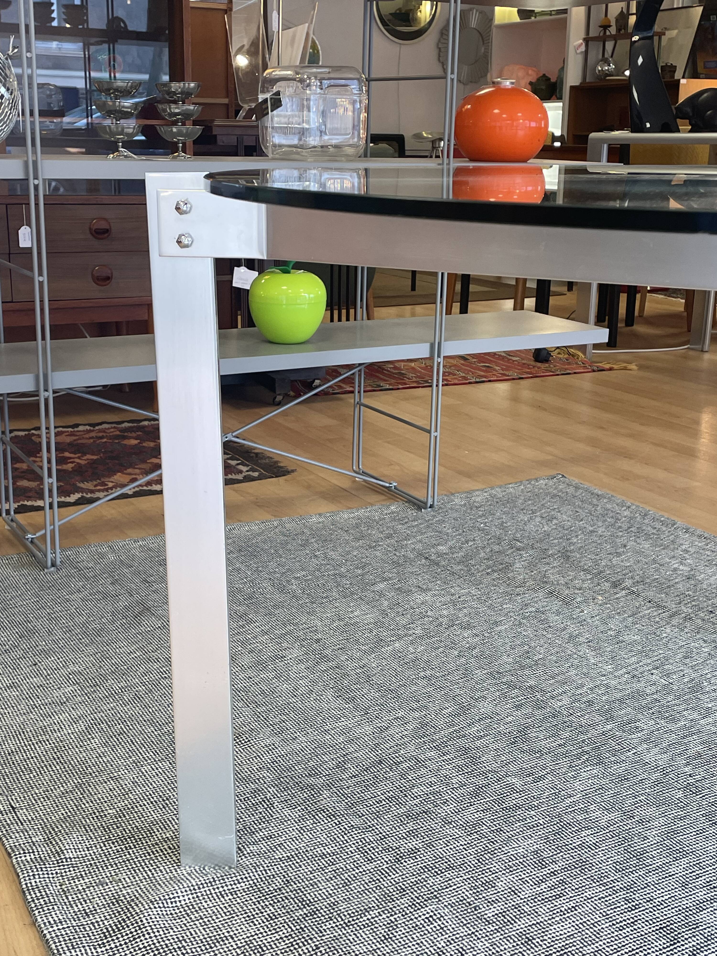 Round dining table with a glass top and brushed metal triangular frame.