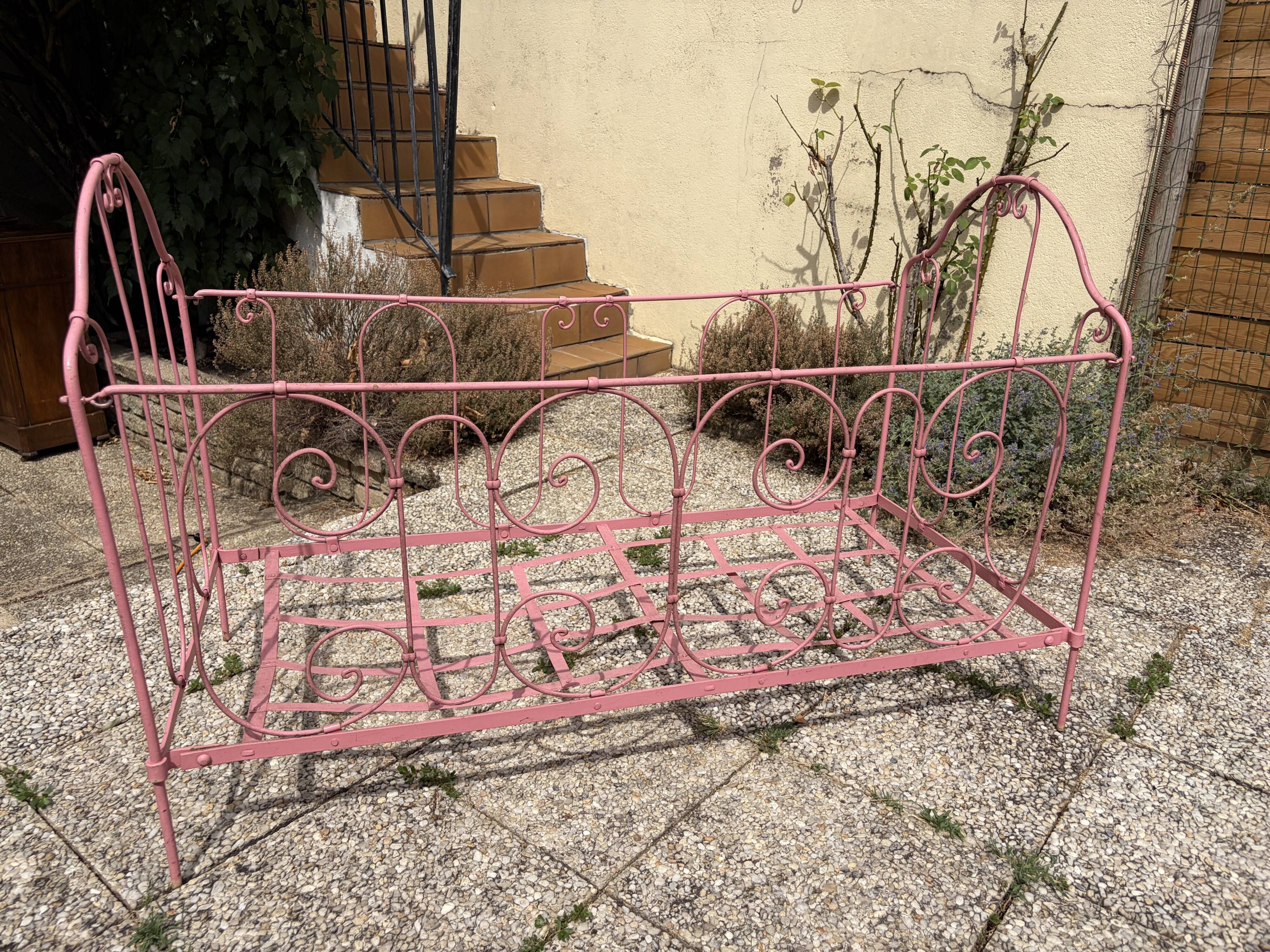 Old iron bed for children, painted pink with scrolls, romantic style.