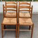 4 solid wood kitchen chairs with straw seats in a country farmhouse style.