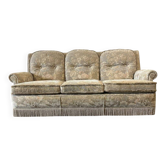Vintage beige three-seater sofa with floral pattern and fringes.