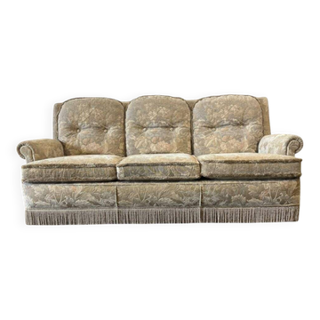 Vintage beige three-seater sofa with floral pattern and fringes.