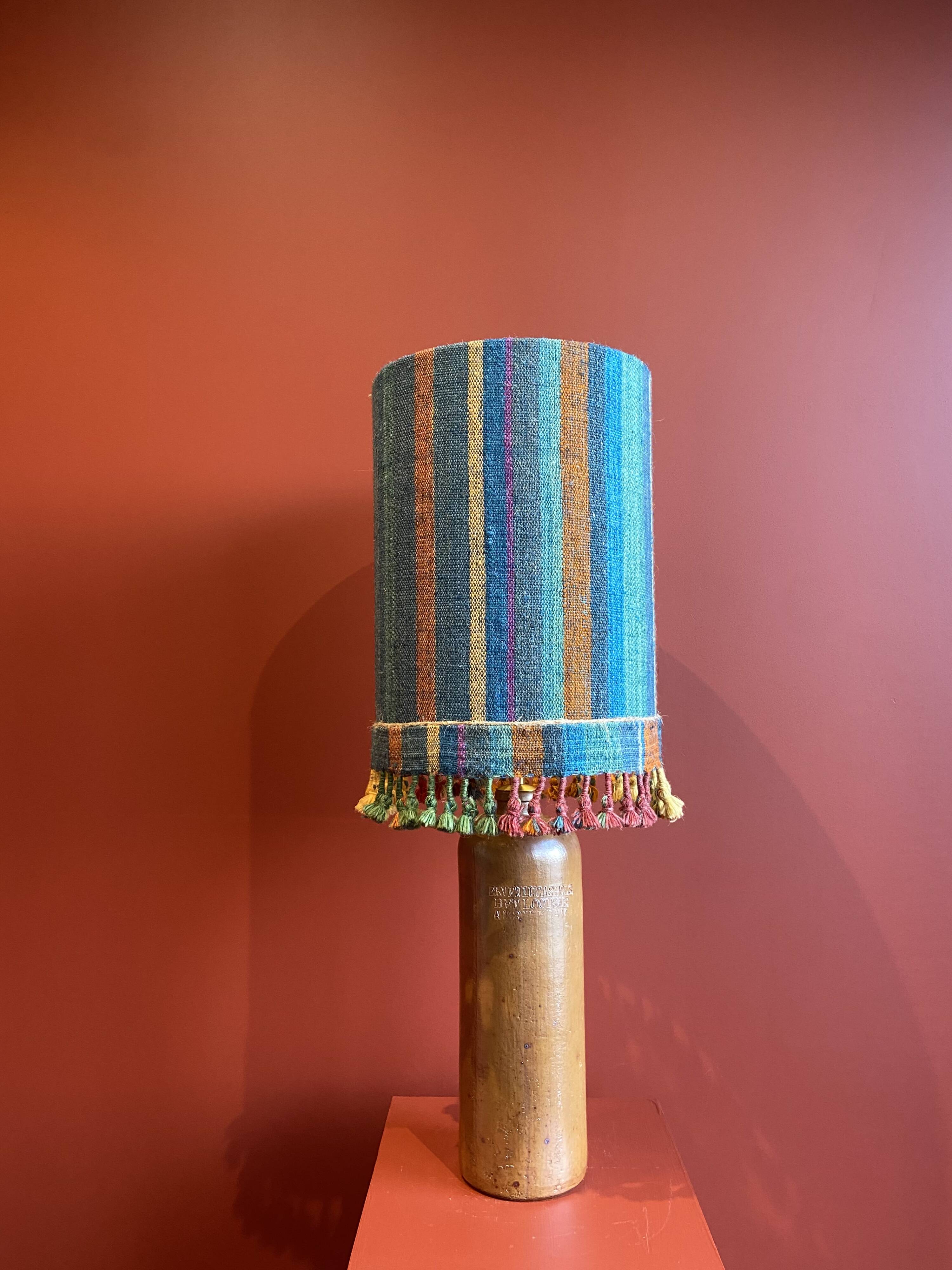 "Stoneware Bottle Lamp" with a multicoloured blue lampshade handwoven in India.