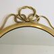 Decorative oval mirror in brass adorned with a large twisted bow.