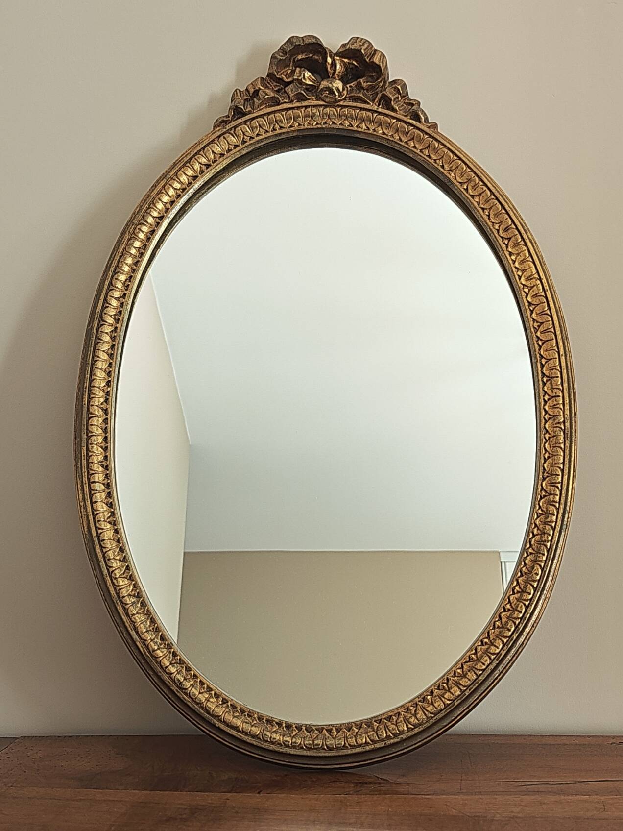 Vintage oval mirror with a carved wooden frame in gold, decorated with a bow.