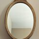 Vintage oval mirror with a carved wooden frame in gold, decorated with a bow.