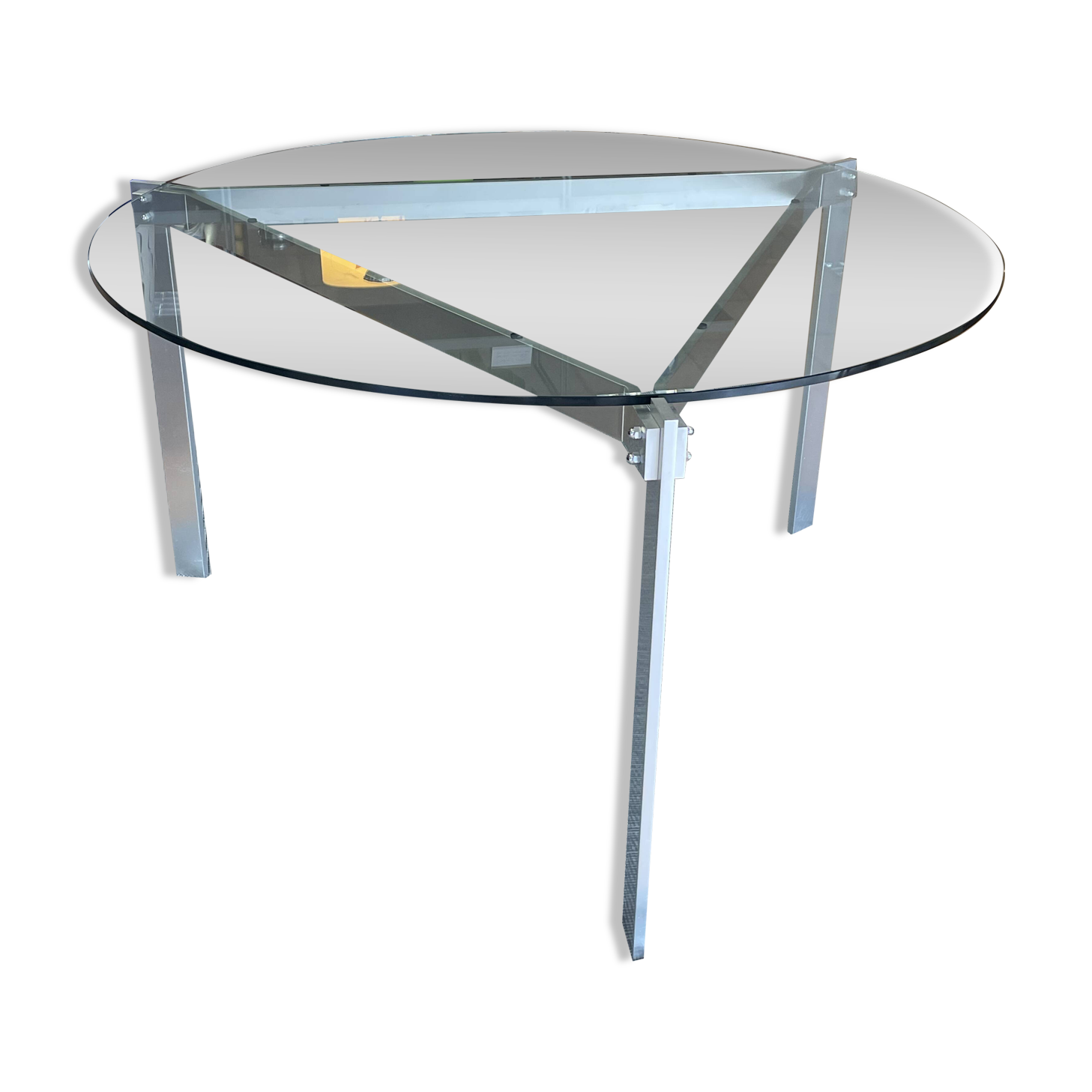 Round dining table with a glass top and brushed metal triangular frame.