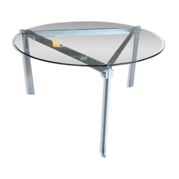 Round dining table with a glass top and brushed metal triangular frame.