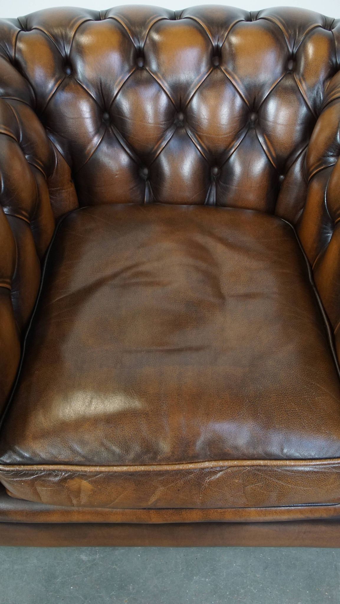 A well-maintained cowhide leather English Chesterfield armchair