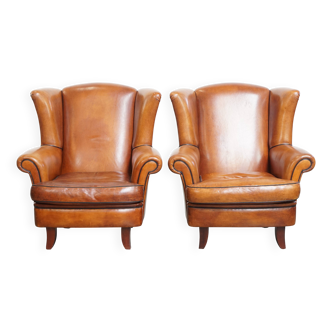 2 fauteuils à oreilles en cuir de mouton et passepoil noir