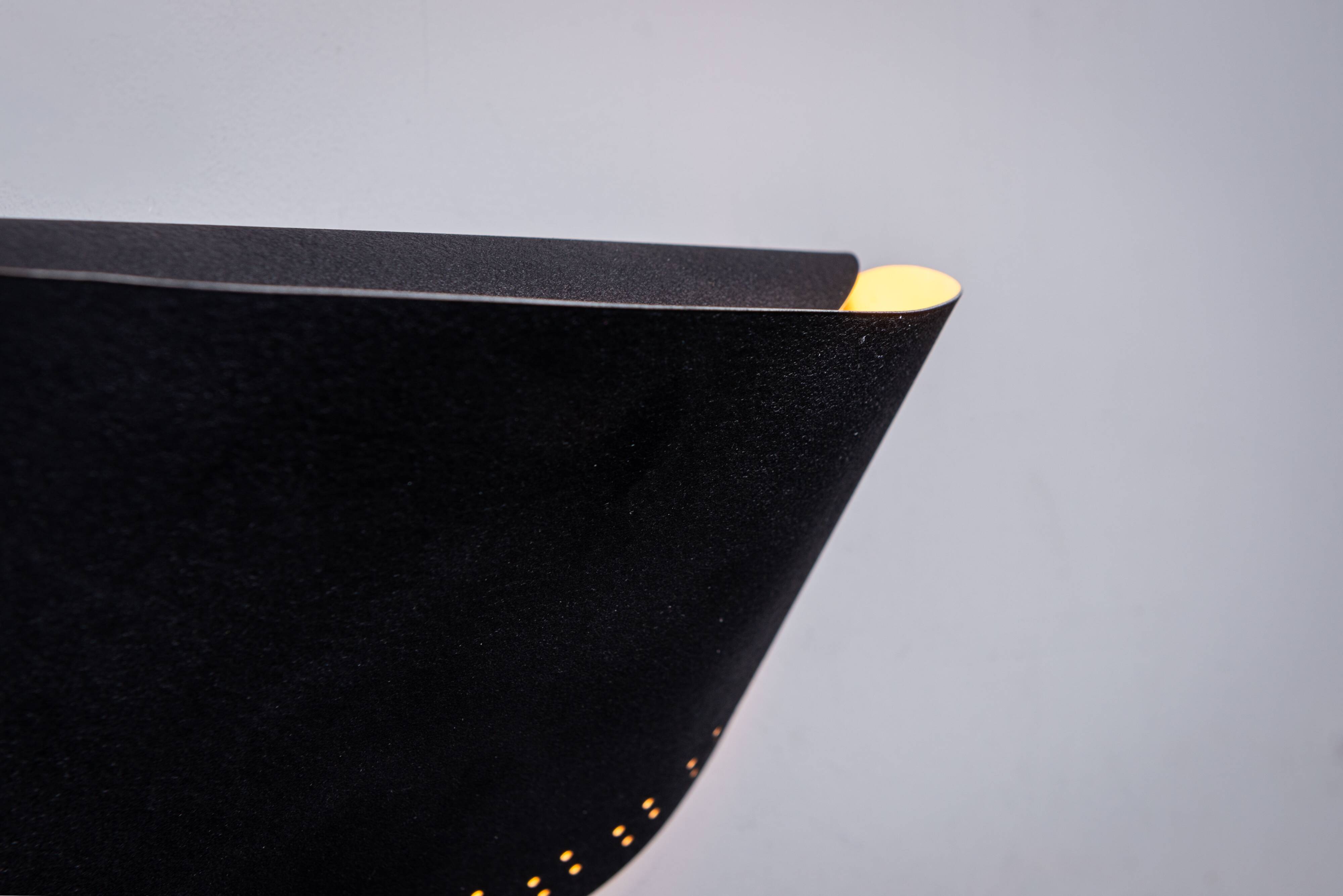 Matte black wall lamps with perforated shades and brass details