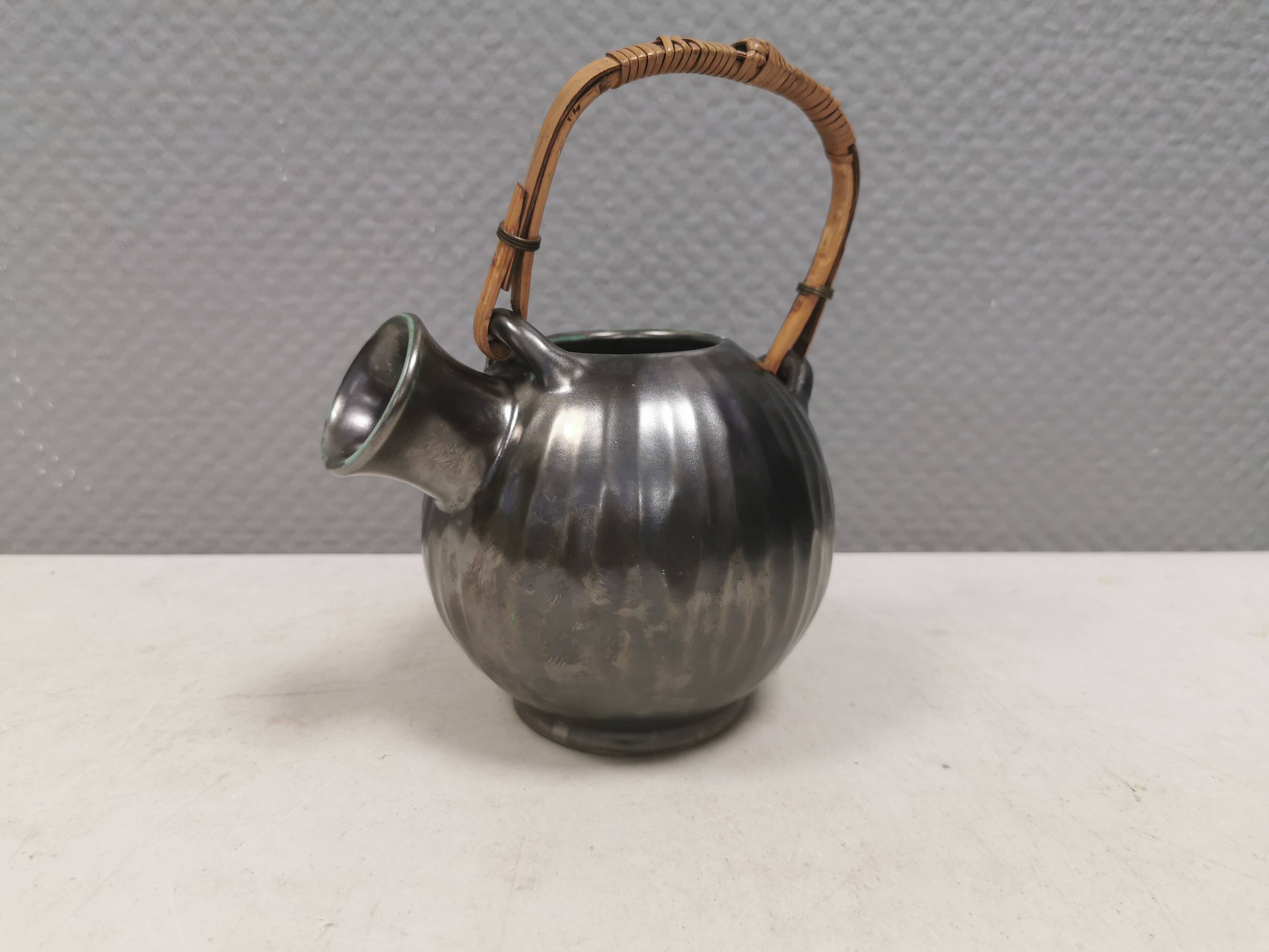 A ceramic jug with a metallic glaze and a handle made of woven raffia.