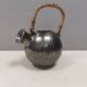 A ceramic jug with a metallic glaze and a handle made of woven raffia.