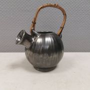 A ceramic jug with a metallic glaze and a handle made of woven raffia.