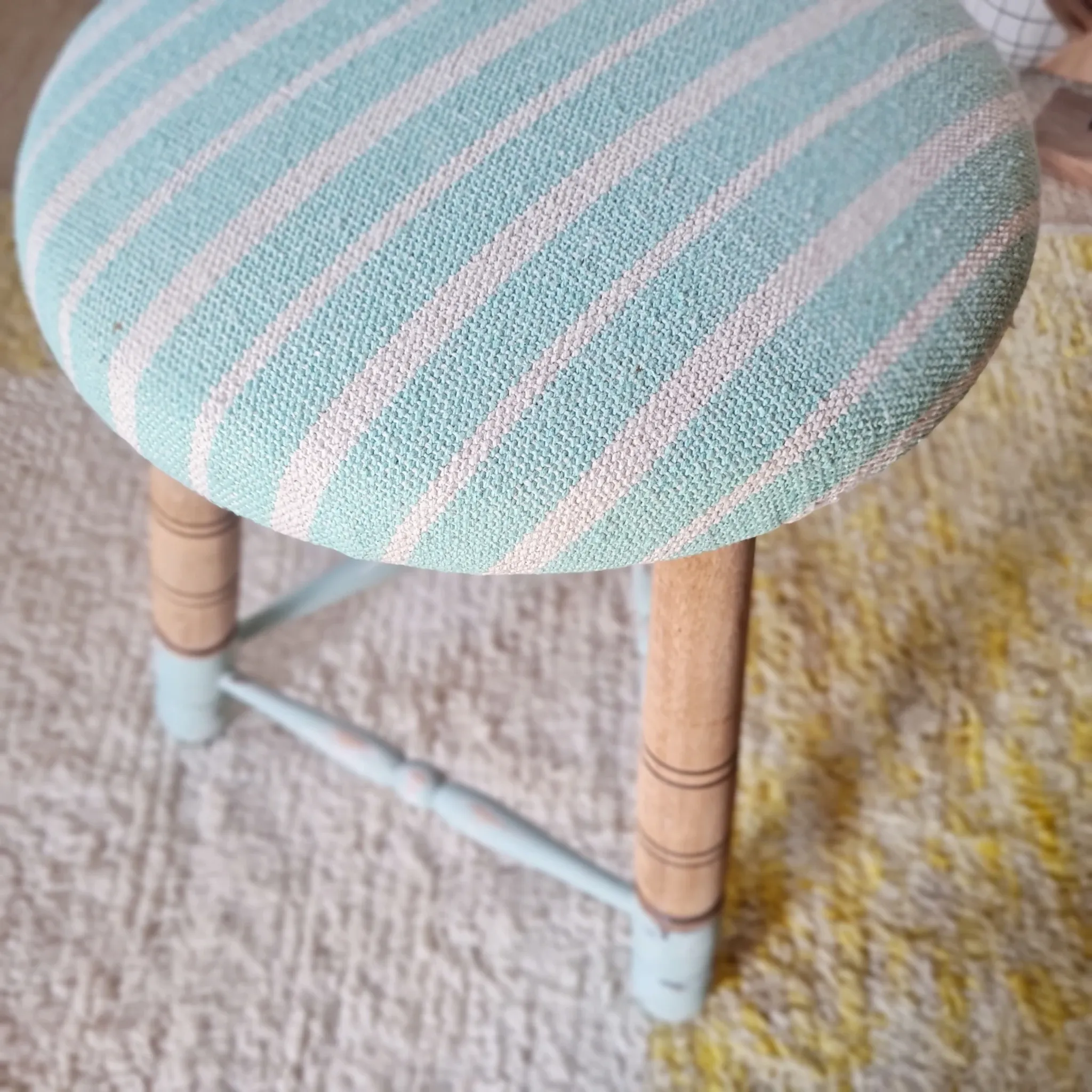 Antique tripod stool with blue striped seat.