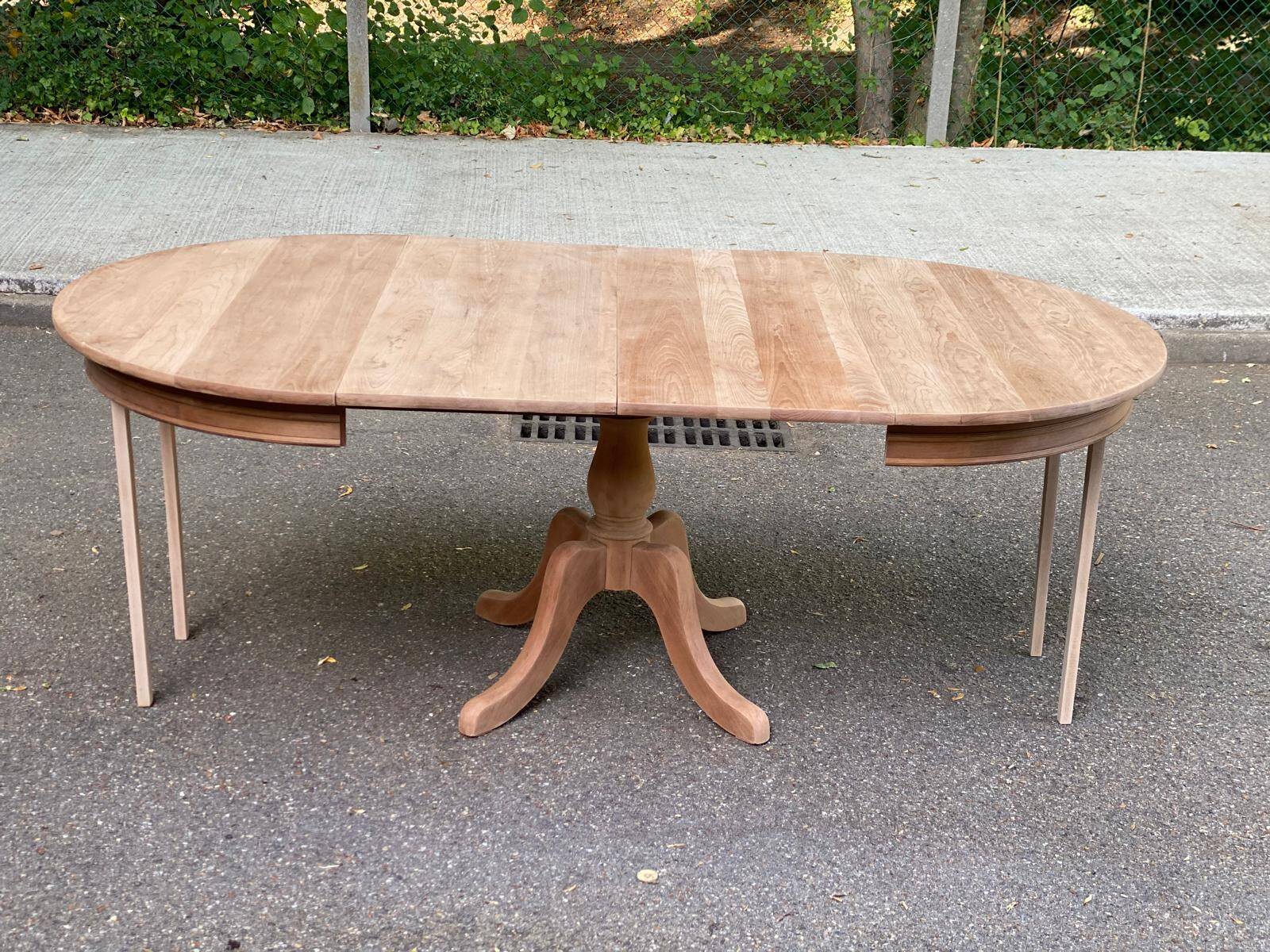 Large extendable round dining table stripped in solid cherry wood with a central leg.
