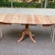 Large extendable round dining table stripped in solid cherry wood with a central leg.