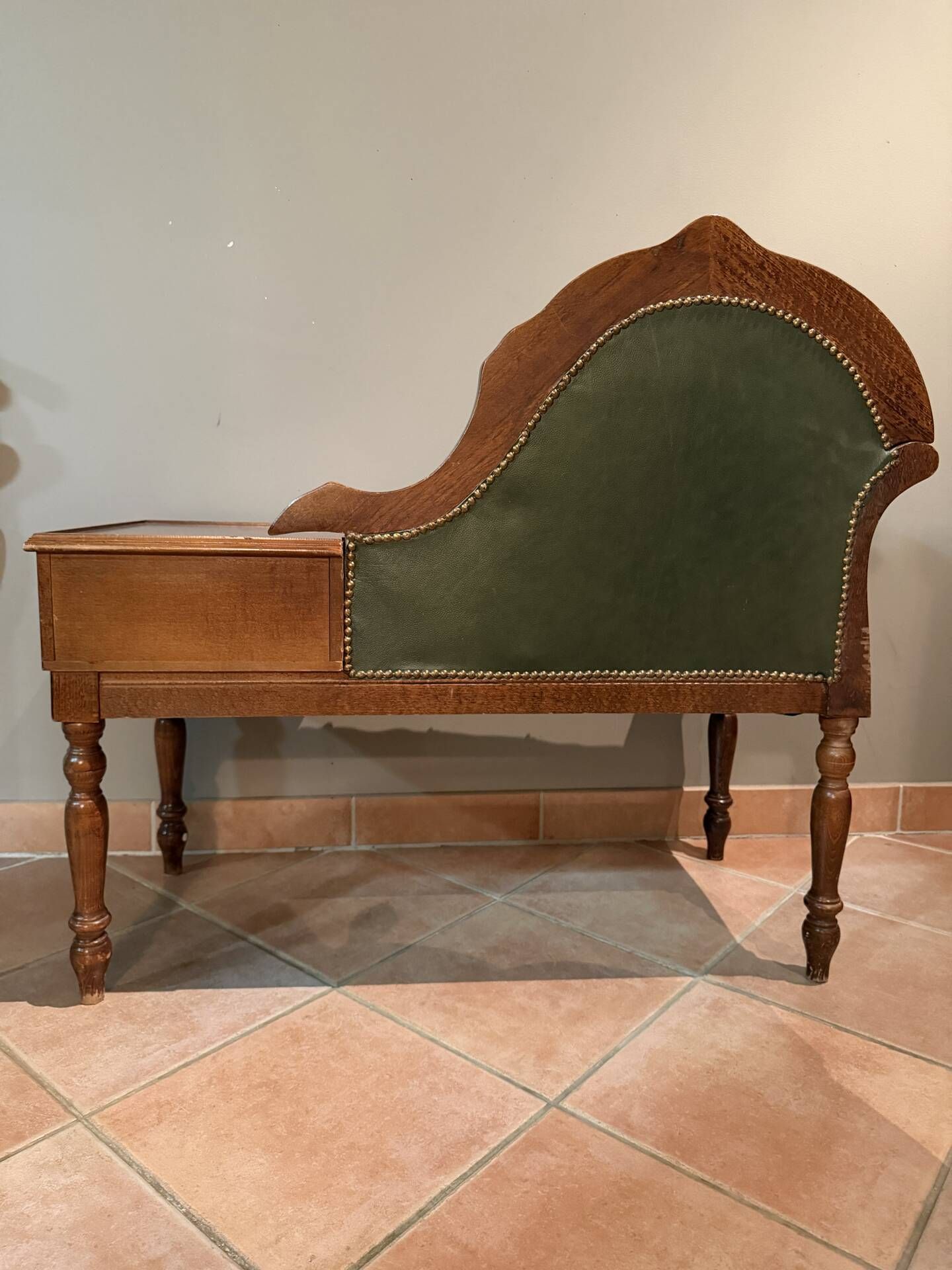 Antique carved wooden bench with green upholstered seat and backrest.