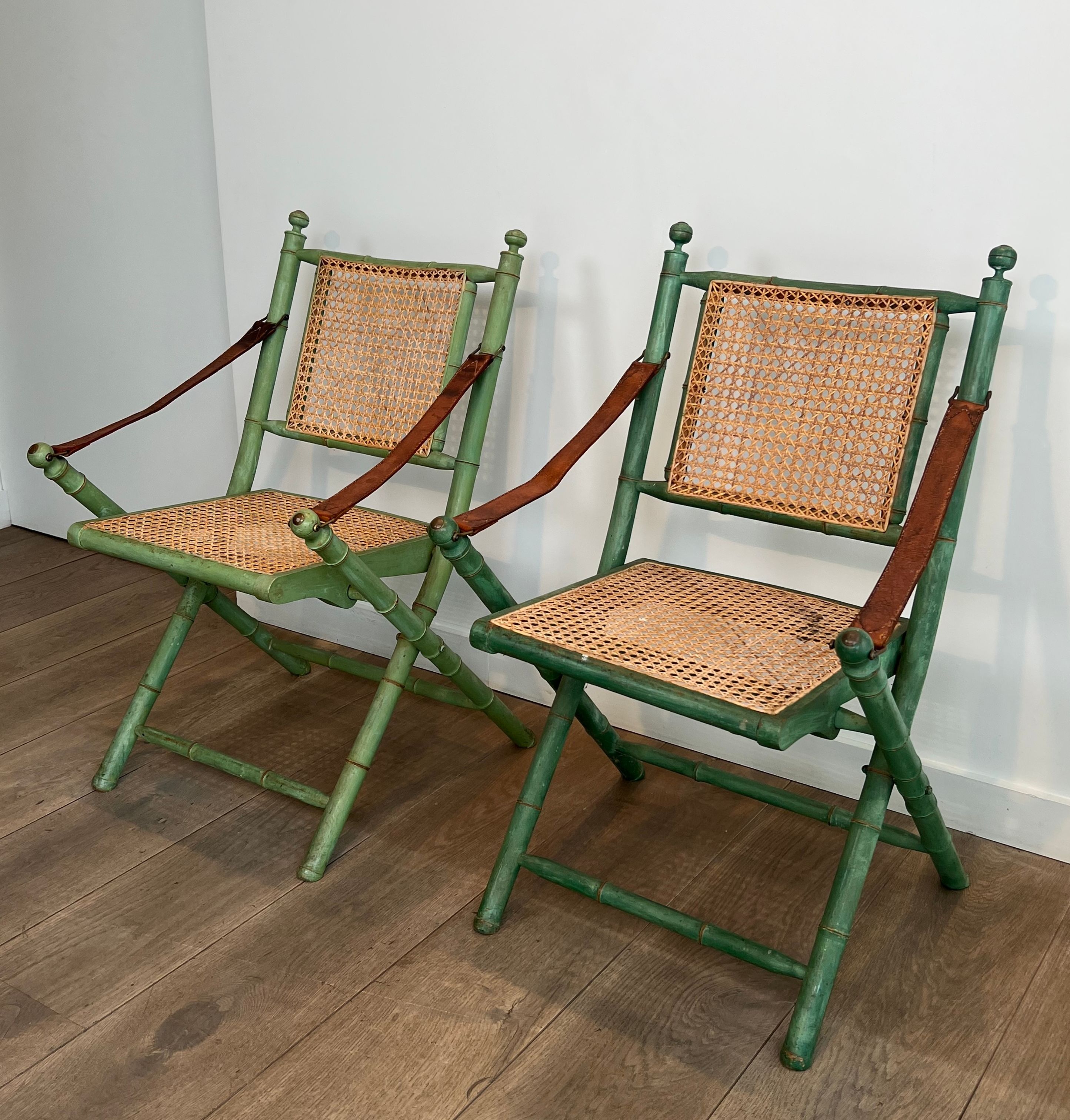 Paire de chaises safari pliantes façon faux-bambou patiné, dossiers et assises cannées et repose-bras en cuir