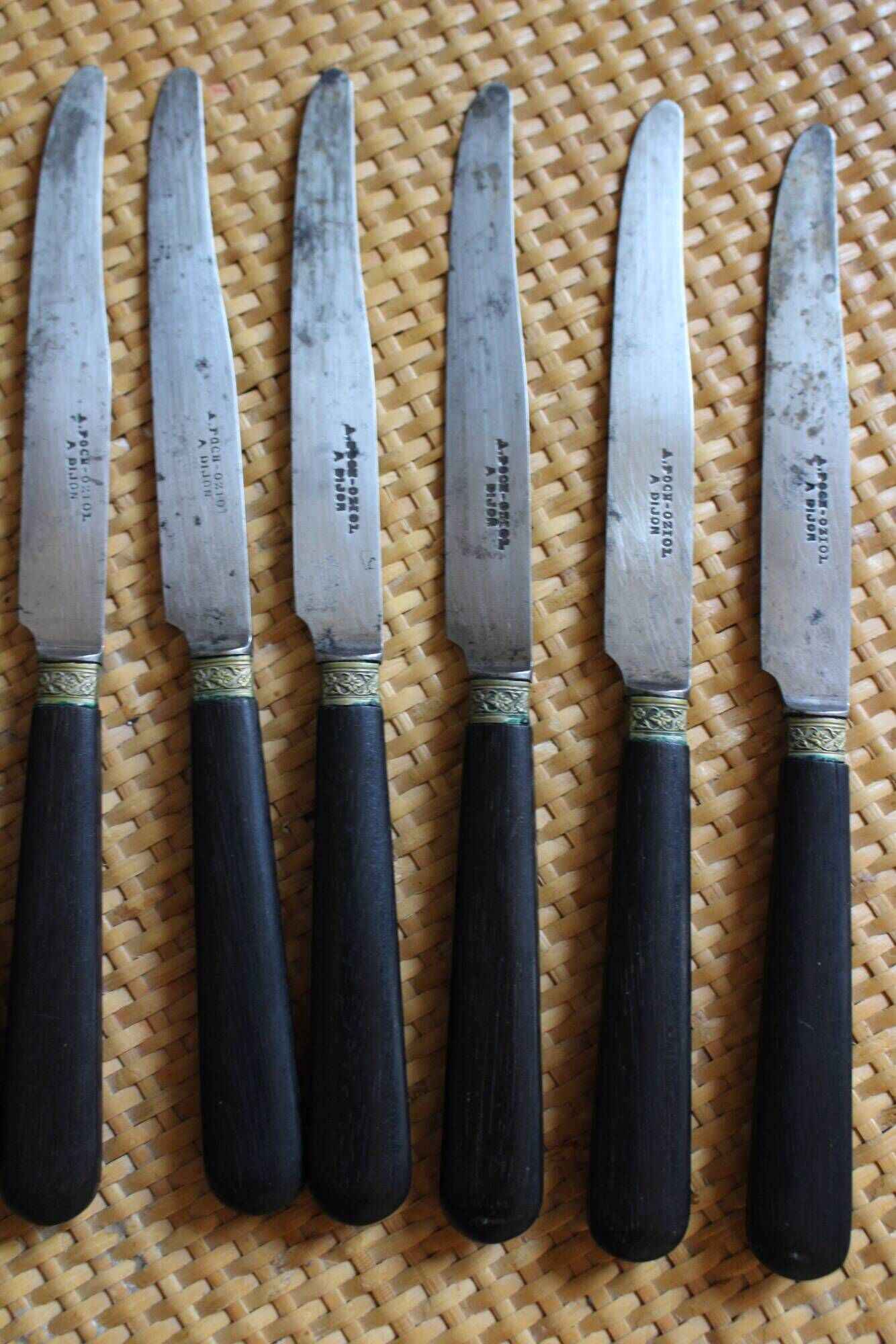 A set of 8 knives with black wooden handles and bolsters.