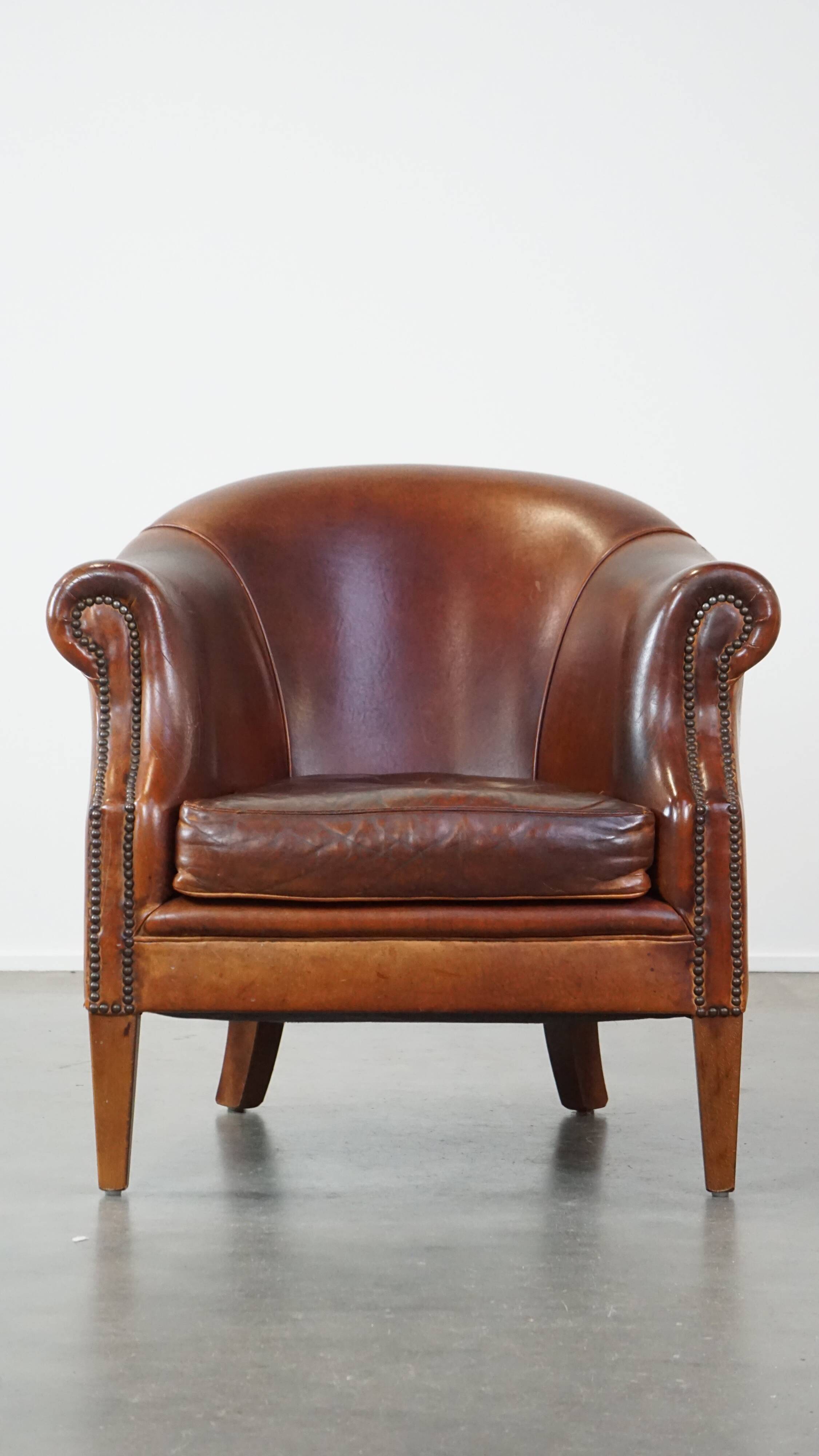 Un fauteuil club robuste mais confortable en cuir de mouton et fini avec des clous décoratifs