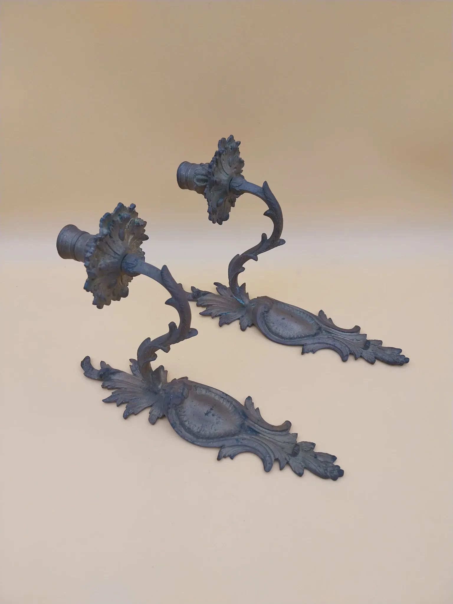 Pair of wall sconces in bronze candle holders with leaf medallion decoration.