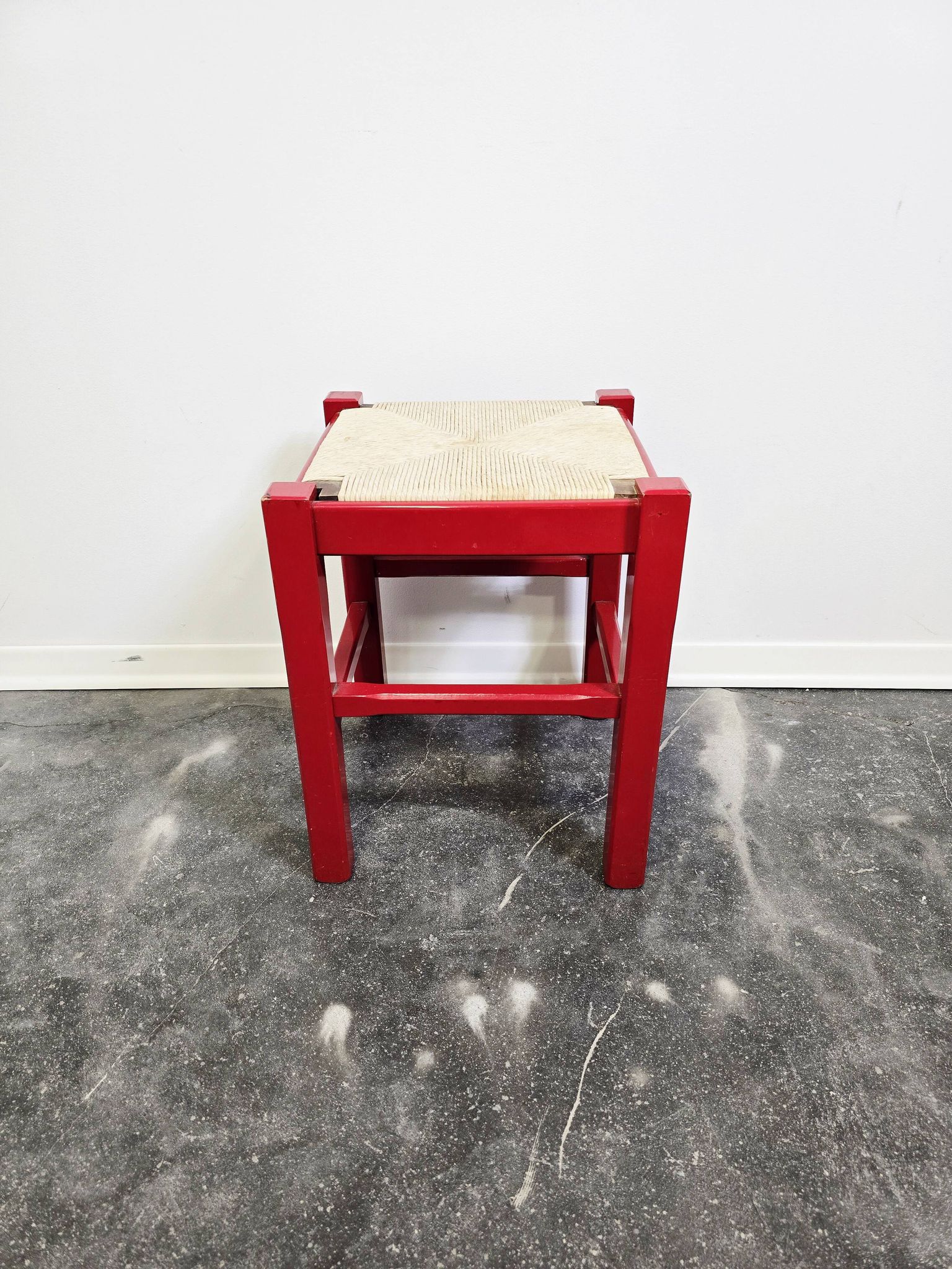 Red wooden stool with a woven straw seat.