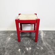Red wooden stool with a woven straw seat.