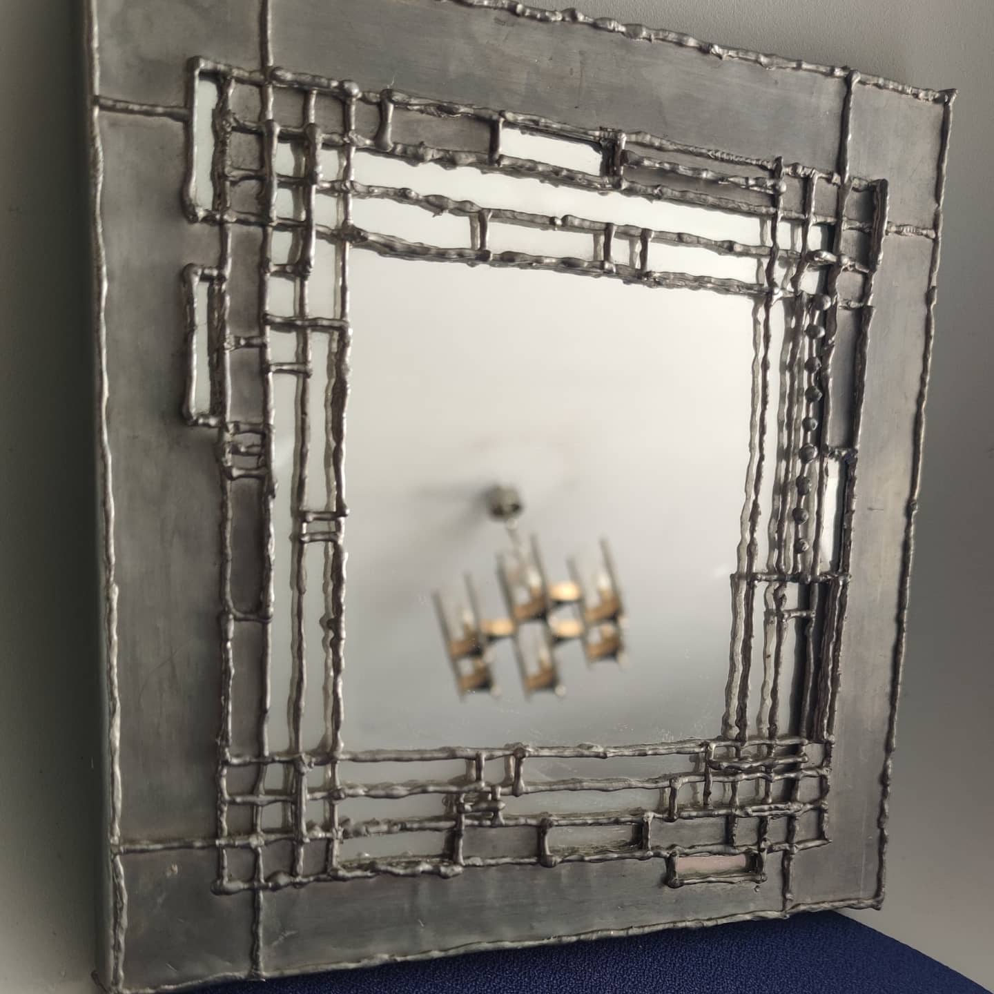 Pewter mirror on a brutalist-style wooden stand