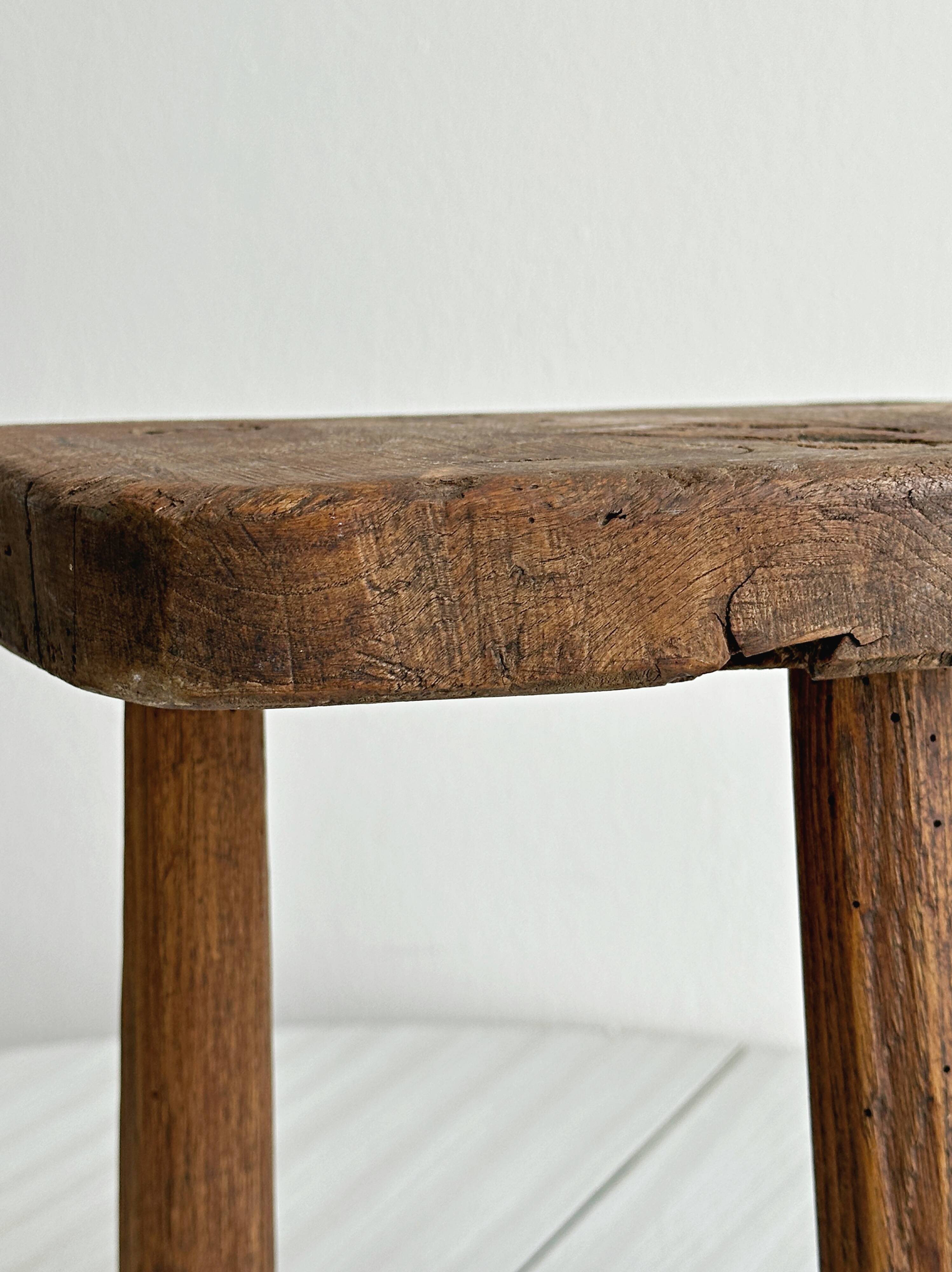 Antique three-legged stool made of raw solid wood.