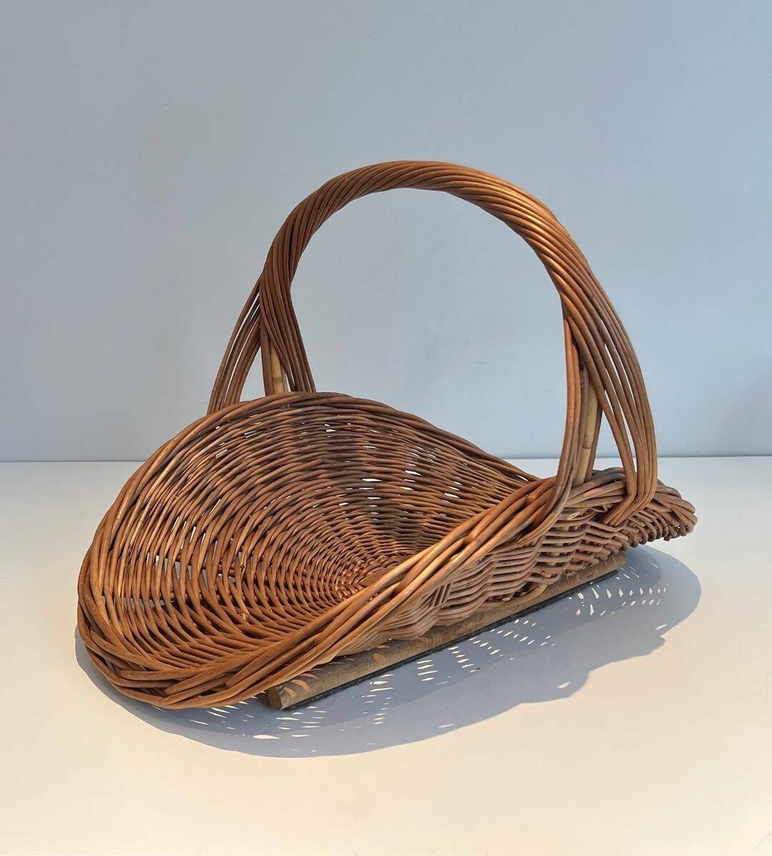 Woven Rattan Log Holder in a Semi-Round Shape with a Central Arched Handle.