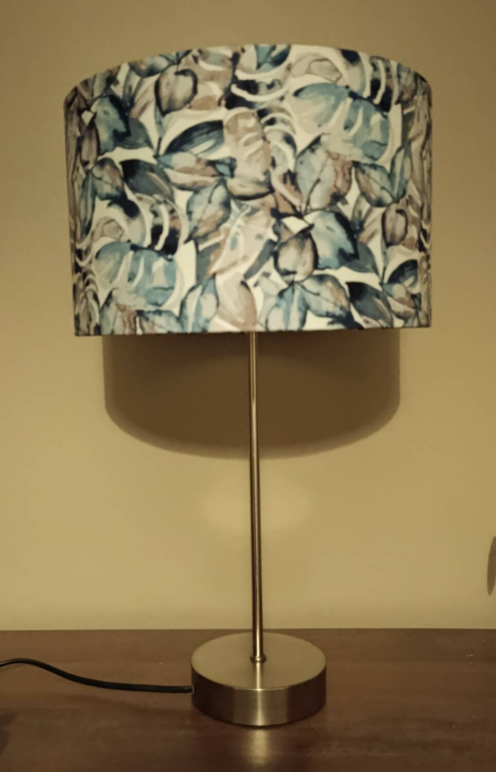 Table lamp with chrome stem, tropical plant shade.