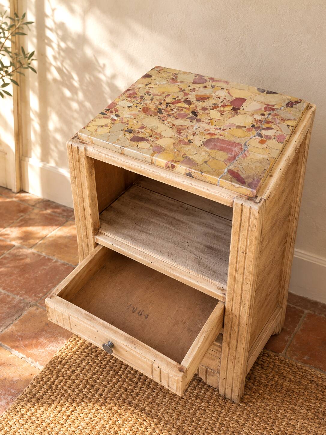 Small Art Deco bedside table in light wood with a terrazzo effect top.