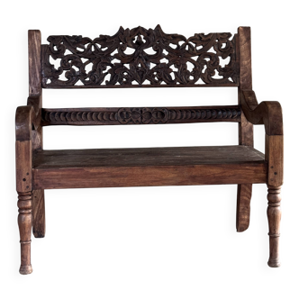 Small antique Indonesian bench in carved teak with plant and floral motifs.
