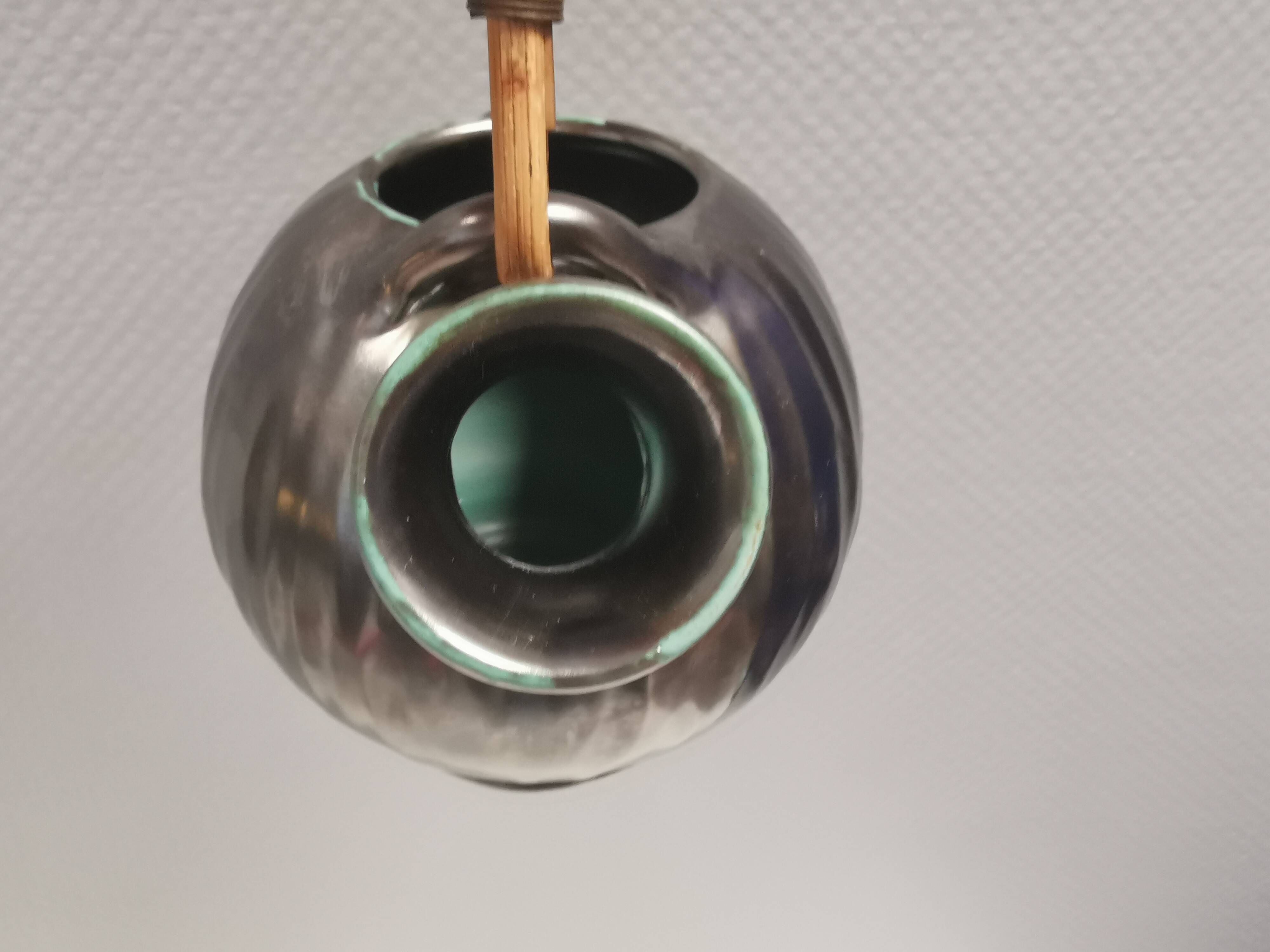 A ceramic jug with a metallic glaze and a handle made of woven raffia.