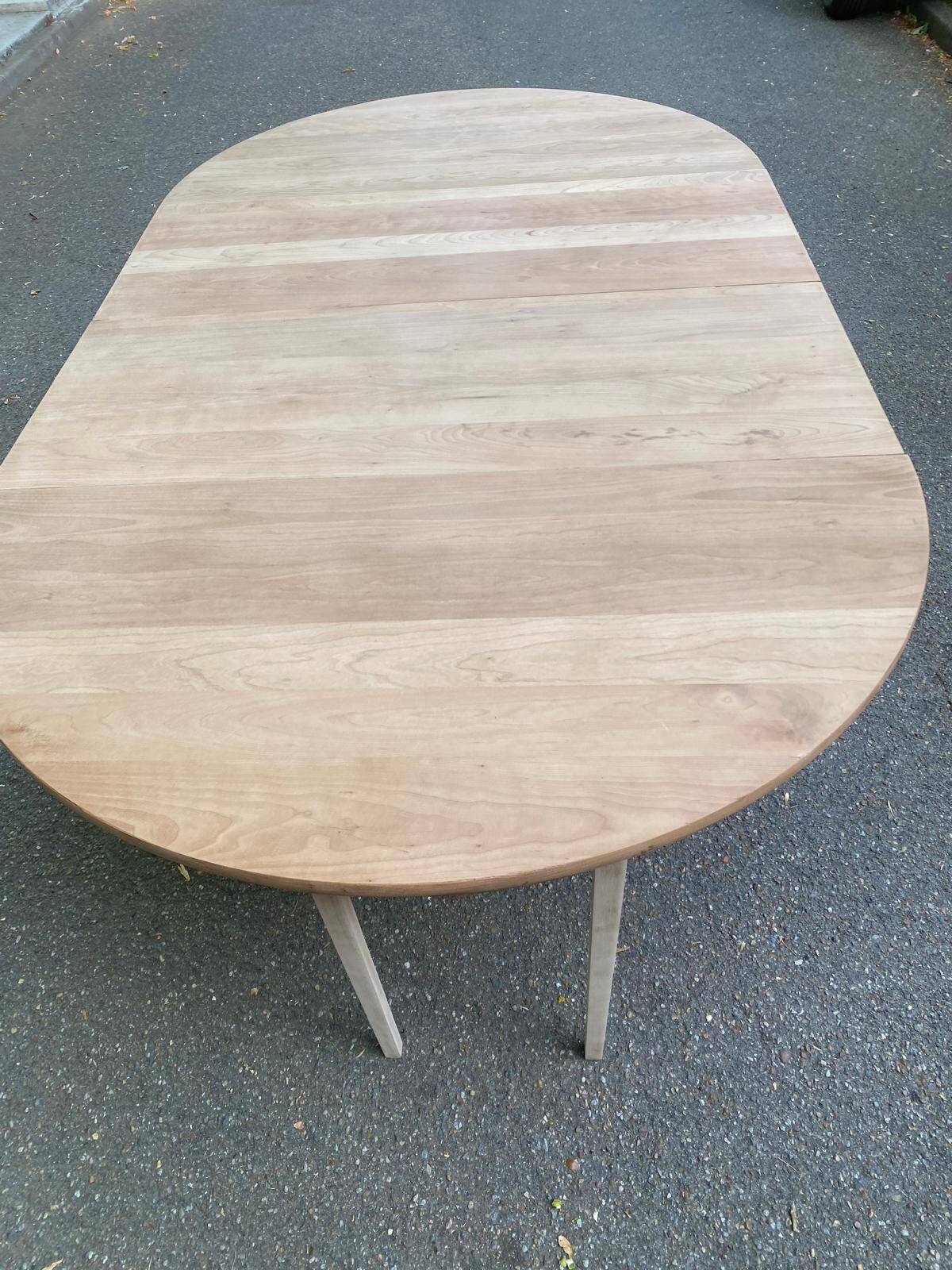 Large extendable round dining table stripped in solid cherry wood with a central leg.